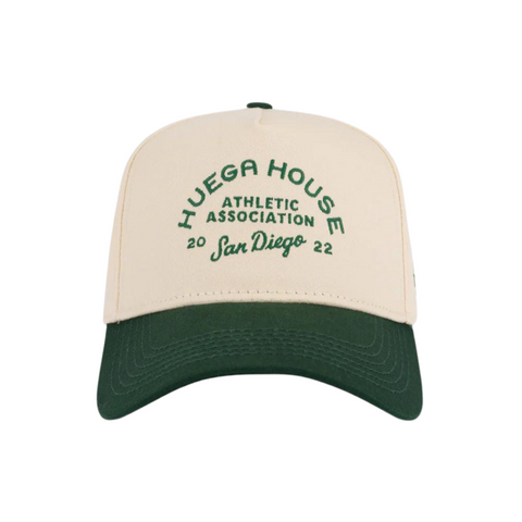 Front view of Huega House Athletic Association Hat in Green and Natural featuring vintage-style embroidered text on a structured green crown with a natural curved brim