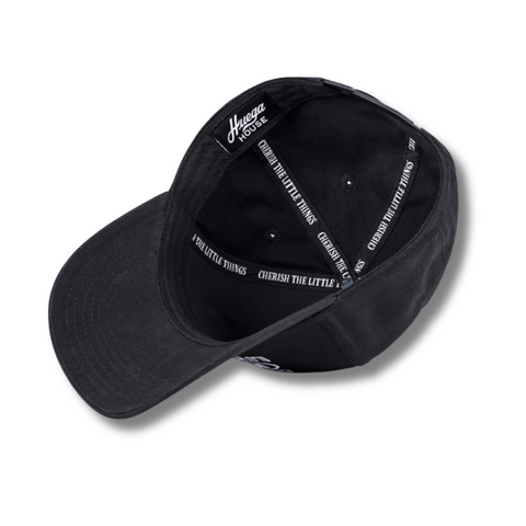 Flat lay of Huega House Circuit Hat in Black highlighting the tonal front logo, flat brim, and performance-inspired construction