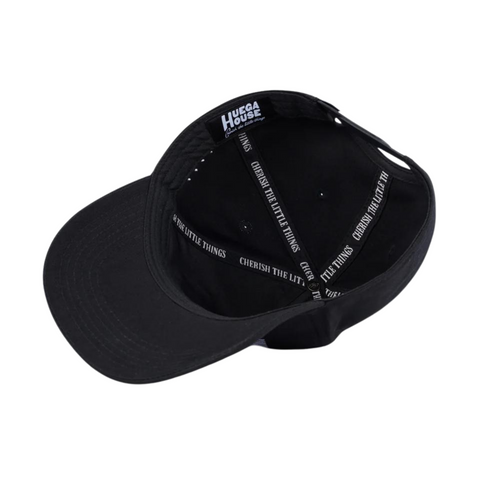 Flat lay of Huega House Legacy Hat in Black highlighting minimalist embroidered logo, soft crown, and pre-curved brim