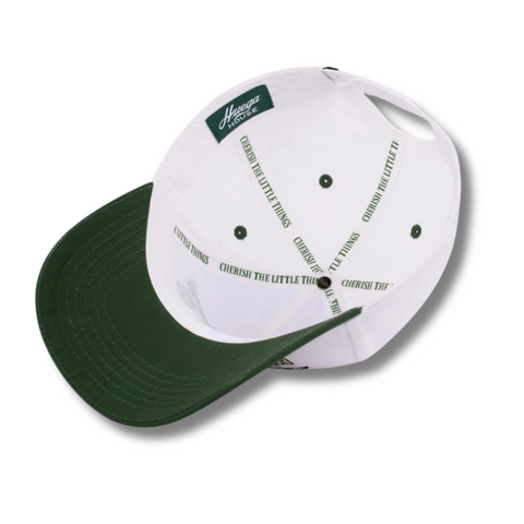 Flat lay of Huega House Moments Hat in Pine Green/White highlighting front “Moments” embroidery, white brim, and crisp structured fit