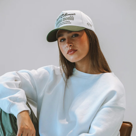 Person wearing the Huega House Moments Hat in Pine Green and White in a relaxed, nature-inspired outdoor setting