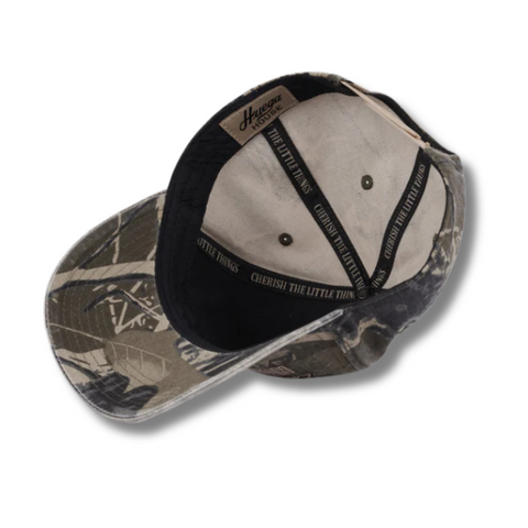 Flat lay of Huega House Moments Hat in Vintage Camo highlighting embroidered text, curved brim, and classic camo color palette