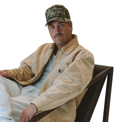 Person wearing the Huega House Moments Hat in Vintage Camo in a rugged, nature-inspired or casual weekend setting