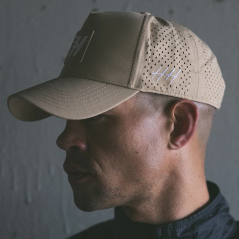 Person wearing the Huega House Success Performance Hat in Khaki in an outdoor, active, or travel-ready setting