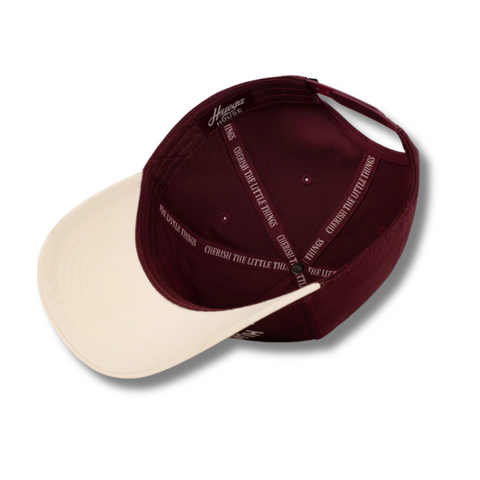 Flat lay of Huega House Trademark Hat in Natural/Maroon highlighting embroidered logo, curved brim, and premium contrast design