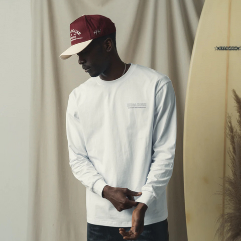 Person wearing the Huega House Trademark Hat in Natural and Maroon in a relaxed, casual setting