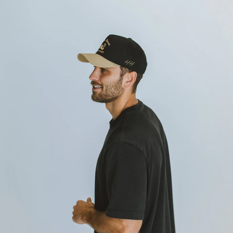 Person wearing the Huega House Vintage Swan Hat in Black and Khaki in a laid-back, outdoorsy or weekend setting