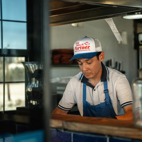 Person wearing the Sendero Easy Does It Hat in White and Red in a relaxed outdoor or Western-inspired setting
