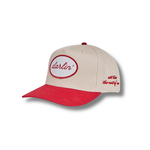 Side view of DARLIN'® Snapback in Cream/Red showing curved red brim, cream front panel, and high-contrast white patch