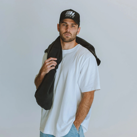 Person wearing the Huega House Legacy Hat in Black in a casual, urban setting or outdoor environment