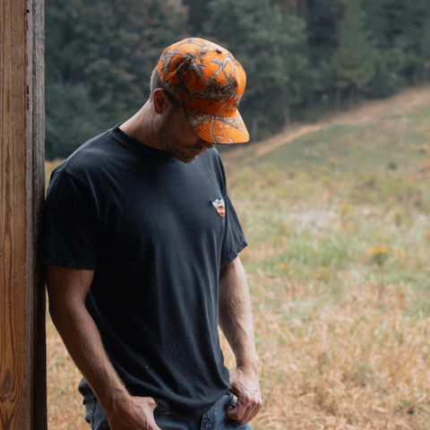 Person wearing the Melin Odyssey Real Tree Hydro Hat in Neon Camo in an active, outdoor adventure setting