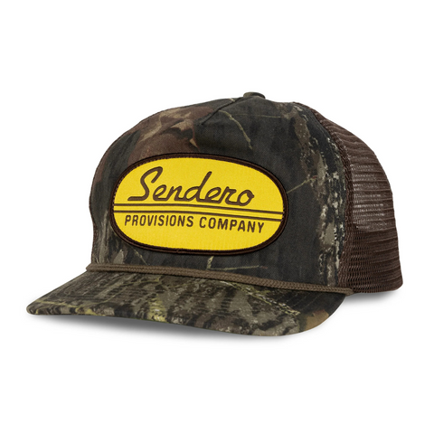 Side view of Sendero Country Store Hat in camo showing Mossy Oak-style print, mesh back panel, and trucker fit
